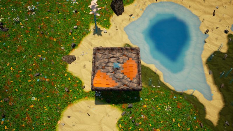 Top-down view of a stone basin holding lava, beside a blue lake and grassland.